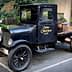 A vintage black pickup truck with wooden barrels in the back, parked on a paved surface. - Olive Oil Times