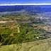 Aerial view showing extensive agricultural fields and mountainous terrain under a clear sky. - Olive Oil Times