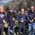 Four men standing in an olive grove, each holding a bottle of olive oil. - Olive Oil Times