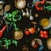 An overhead view of various cooking ingredients including vegetables, herbs, and spices on a wooden surface. - Olive Oil Times