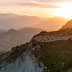 Blick auf den Sonnenuntergang über einer Berglandschaft mit sanften Hügeln und Olivenbäumen. - Olive Oil Times