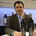 Un homme en costume assis à une table avec deux bouteilles d'huile d'olive devant lui. - Olive Oil Times