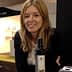 Woman with long blonde hair smiling while holding a bottle of olive oil. - Olive Oil Times