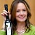 Femme souriante tenant une bouteille d'huile d'olive dans sa main droite. - Olive Oil Times