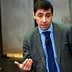 Man wearing a grey suit and blue checkered shirt speaking at an event. - Olive Oil Times