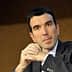 A man in a dark suit with short black hair, sitting with his hands clasped in front of him. - Olive Oil Times