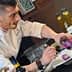 Chef en blouse blanche préparant un plat avec de l'huile d'olive et des ingrédients colorés sur un comptoir. - Olive Oil Times