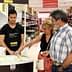 A young man serving olive oil samples to two customers in a store aisle. - Olive Oil Times