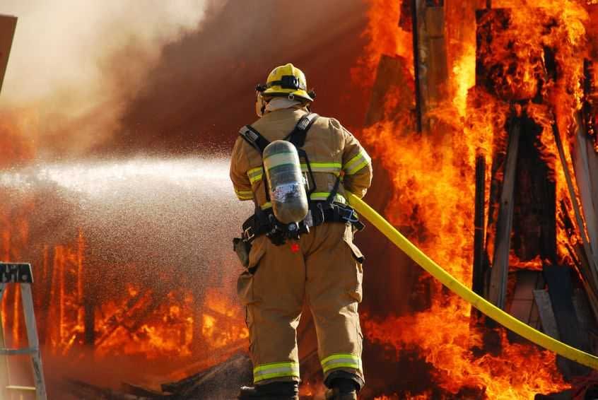 Firefighter in protective gear using a hose to spray water on a large fire. - Olive Oil Times