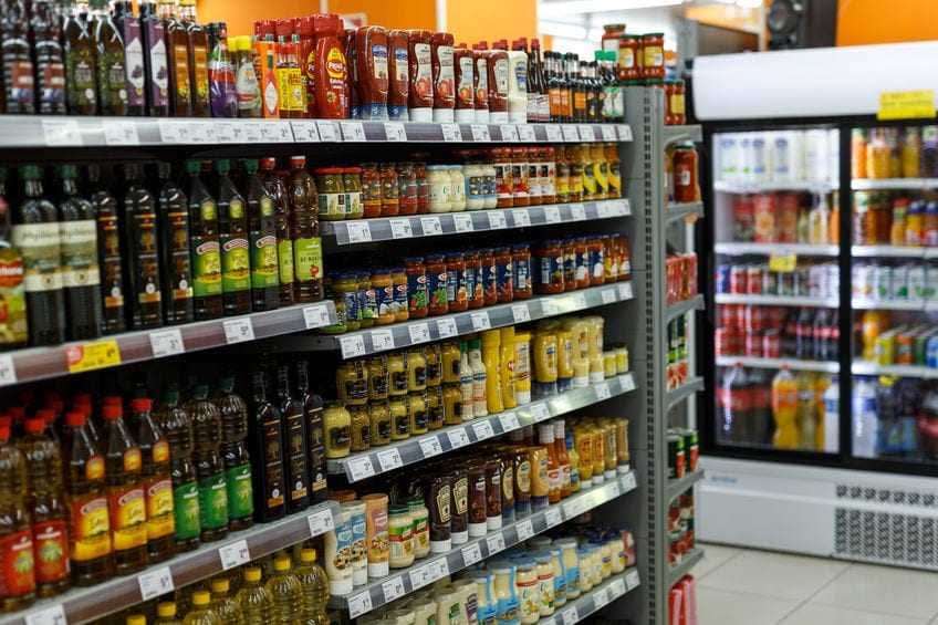 Een gangpad in een supermarkt met verschillende flessen kruiden en bakoliën op planken. Olive Oil Times