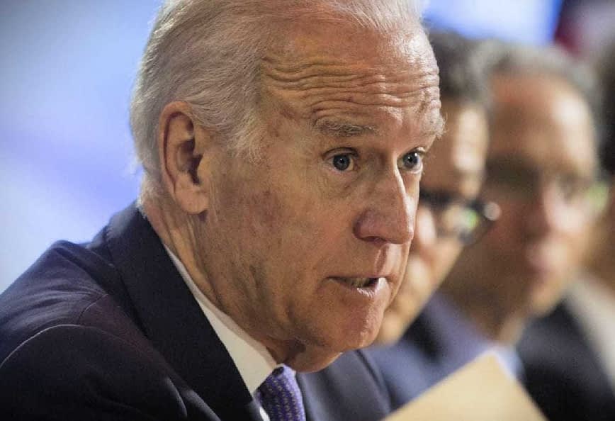 A man in a suit speaking during a conference, holding a document in his hand. - Olive Oil Times