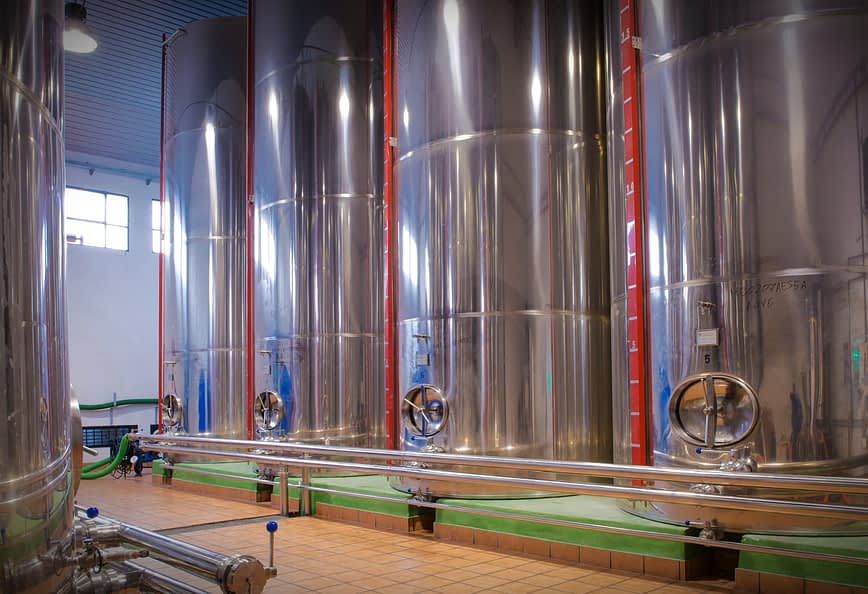 Row of stainless steel fermentation tanks used in winemaking process inside a winery. - Olive Oil Times
