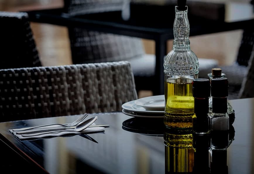 Glass olive oil bottle with a decorative design next to salt and pepper shakers on a table. - Olive Oil Times