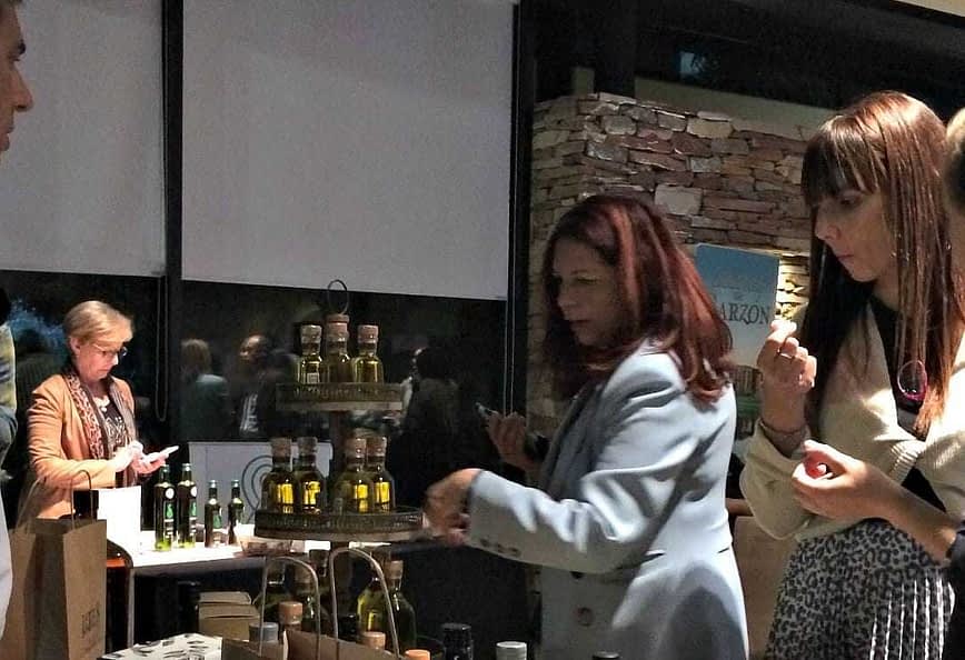 一群人参加橄榄油品尝活动，展示各种橄榄油瓶。 - Olive Oil Times