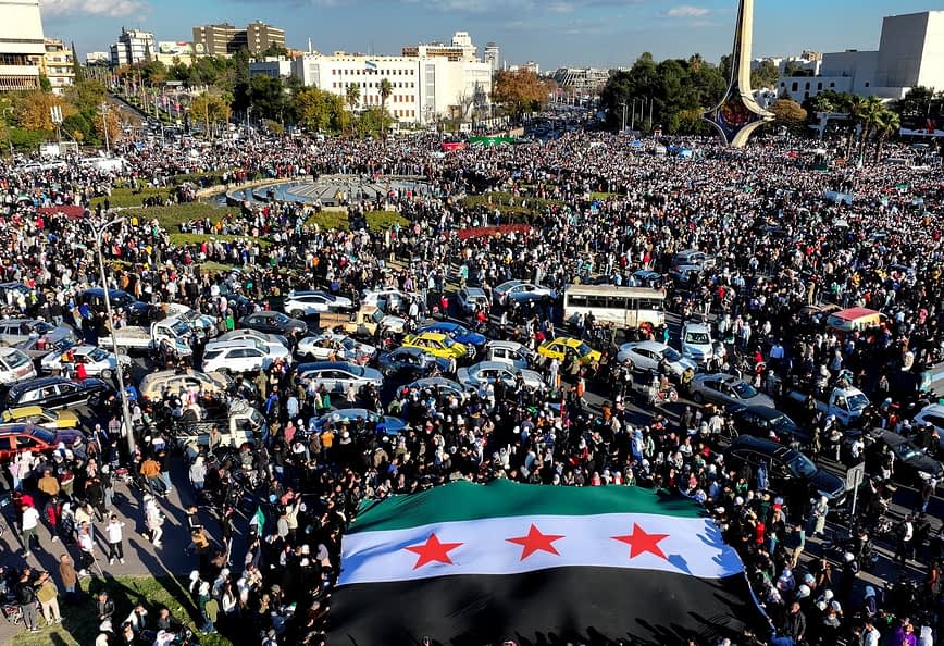 Une grande foule s'est rassemblée sur une place publique tenant un drapeau syrien à trois étoiles. Olive Oil Times