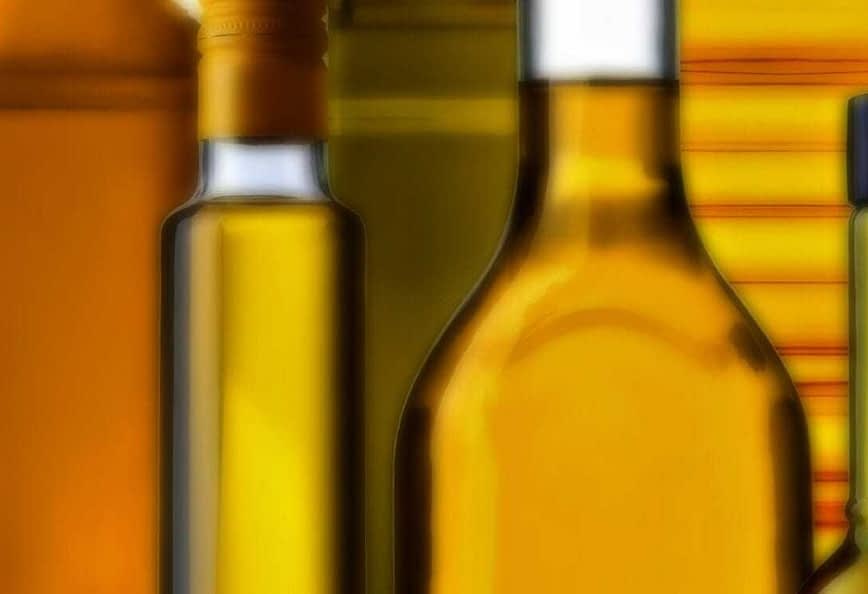 Raccolta di diverse bottiglie di olio di varie forme e colori disposte insieme. Olive Oil Times