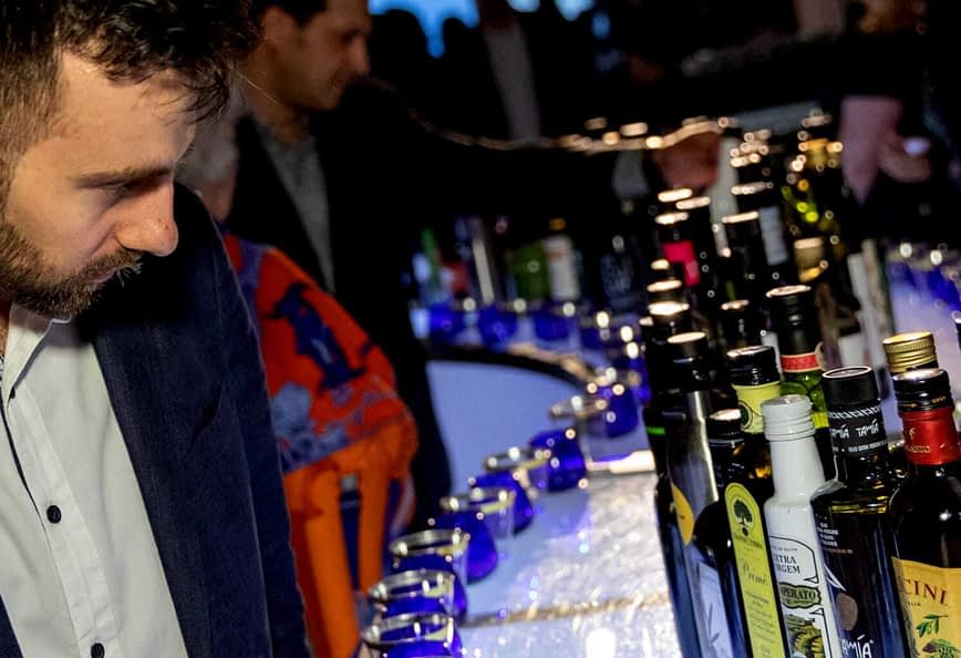 Moški v temni obleki gleda vrsto različnih steklenic na baru na dogodku. - Olive Oil Times
