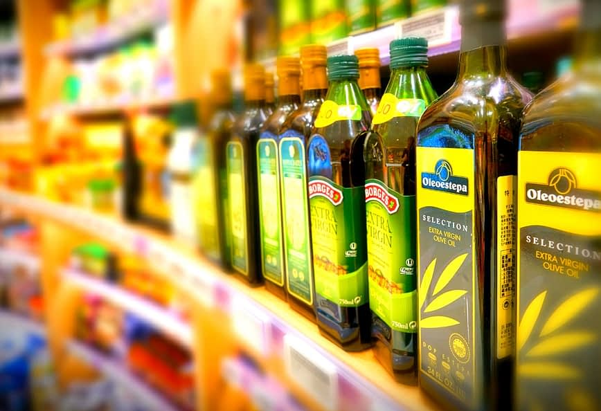 किराने की दुकान के शेल्फ पर जैतून के तेल की विभिन्न बोतलें प्रदर्शित हैं। - Olive Oil Times