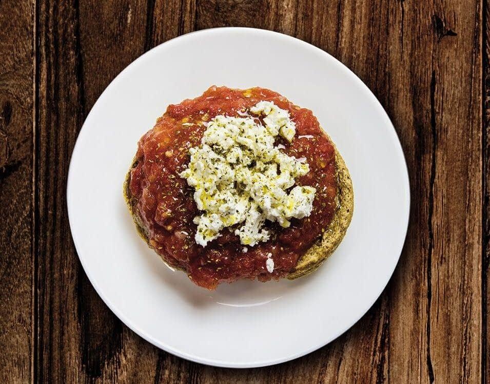 A plate of dakos salad featuring a base of barley rusk topped with tomato sauce and crumbled feta cheese. - Olive Oil Times