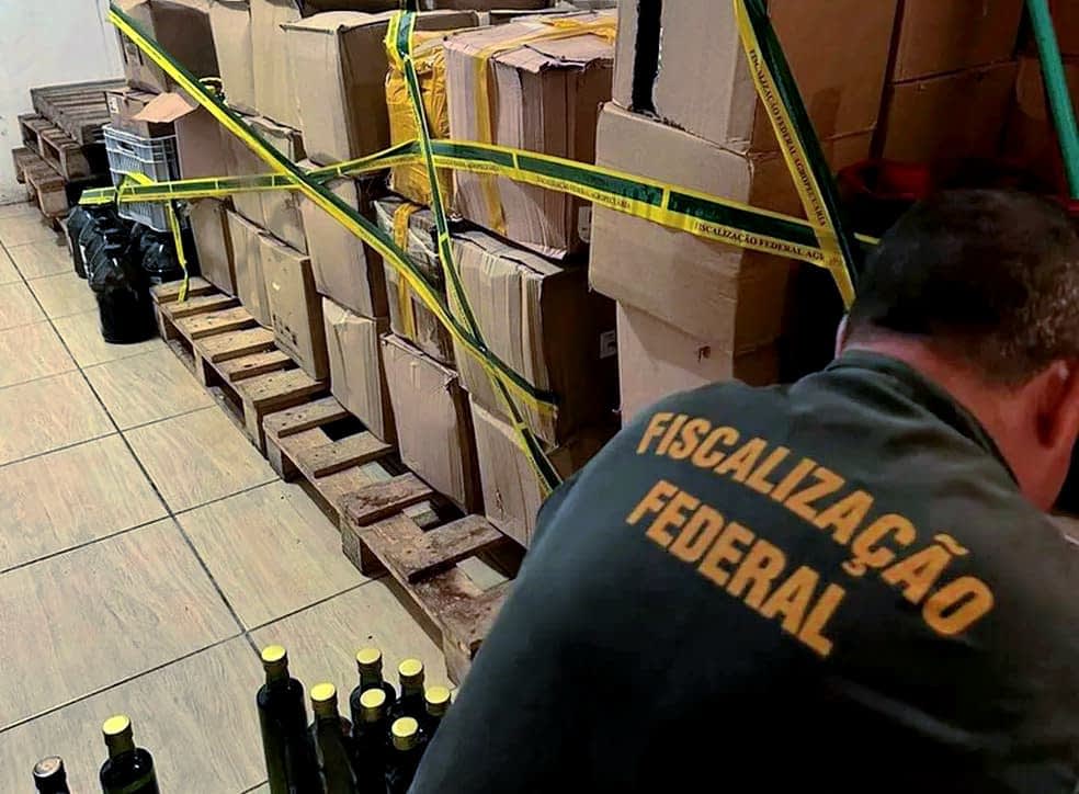 Boxes and bottles secured with yellow tape in a storage area with a person inspecting them. - Olive Oil Times
