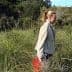 Woman walking through tall grass in a natural outdoor setting with a red bucket. - Olive Oil Times