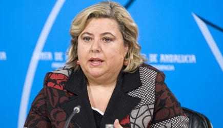 Woman with blonde hair speaking at a press conference in front of a blue backdrop. - Olive Oil Times