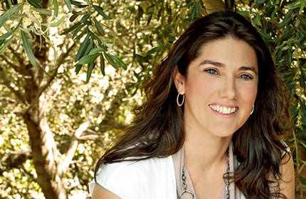 Woman with long dark hair smiling while wearing a white top and earrings. - Olive Oil Times