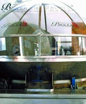 Olive oil mill equipment with a transparent dome showcasing various olive processing materials inside. - Olive Oil Times