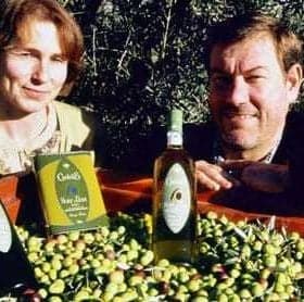 Two individuals posing with bottles of olive oil and a crate of olives in a field. - Olive Oil Times