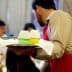 Waiter in a red apron holding a tray with two glasses of colored drinks at a dining event. - Olive Oil Times