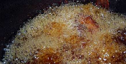 Bubbling oil in a pot during the deep frying process with food submerged. - Olive Oil Times