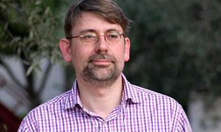 Man wearing a checked shirt with glasses, standing outdoors with a neutral expression. - Olive Oil Times