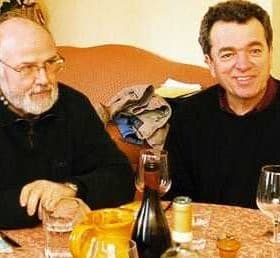 Two men seated at a table with glasses of wine and a bottle in front of them. - Olive Oil Times