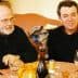Two men seated at a table with glasses of wine and a bottle in front of them. - Olive Oil Times