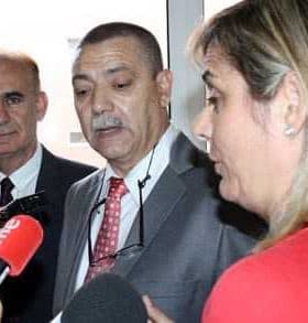 Three individuals, two men and one woman, engaged in a discussion with microphones present. - Olive Oil Times