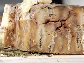 A block of aged cheese with a textured surface placed on a wooden board. - Olive Oil Times
