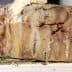 A block of aged cheese with a textured surface placed on a wooden board. - Olive Oil Times