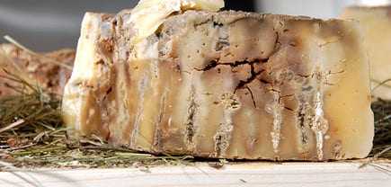 A block of aged cheese with a textured surface placed on a wooden board. - Olive Oil Times