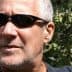 Man with short gray hair wearing sunglasses, with olive trees in the background. - Olive Oil Times