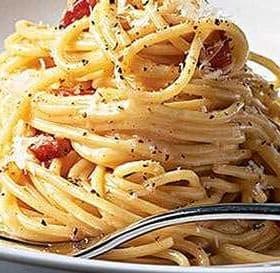 A serving of spaghetti topped with bacon pieces and grated cheese on a white plate. - Olive Oil Times