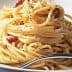 A serving of spaghetti topped with bacon pieces and grated cheese on a white plate. - Olive Oil Times
