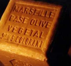 A rectangular bar of Marseille soap with embossed text indicating its olive oil base and natural ingredients. - Olive Oil Times