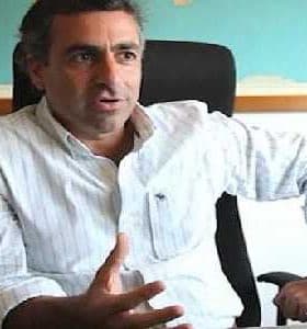 Man with dark hair wearing a white striped shirt sitting in an office chair, gesturing with his hand. - Olive Oil Times