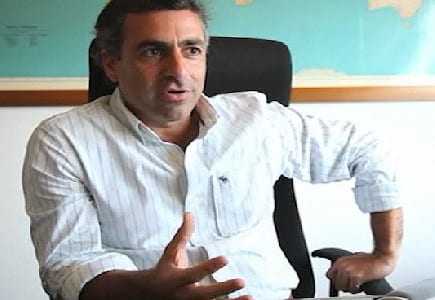 Man with dark hair wearing a white striped shirt sitting in an office chair, gesturing with his hand. - Olive Oil Times