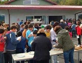A large group of people gathered outdoors at an event, with some individuals serving food at tables. - Olive Oil Times
