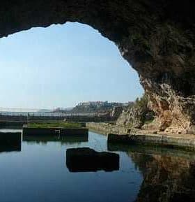View of a cave opening with water reflecting the surrounding rock formations. - Olive Oil Times