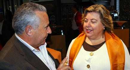 Two individuals, one wearing an orange scarf, engaged in a conversation at an indoor event. - Olive Oil Times