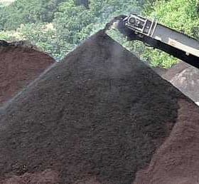 Conveyor belt transferring black soil to a pile in an outdoor setting. - Olive Oil Times