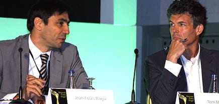 Two men seated at a conference table during a discussion, one wearing a suit and the other in a blazer. - Olive Oil Times