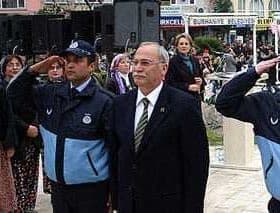 Two police officers saluting alongside a man in a suit at a public event with a crowd in the background. - Olive Oil Times